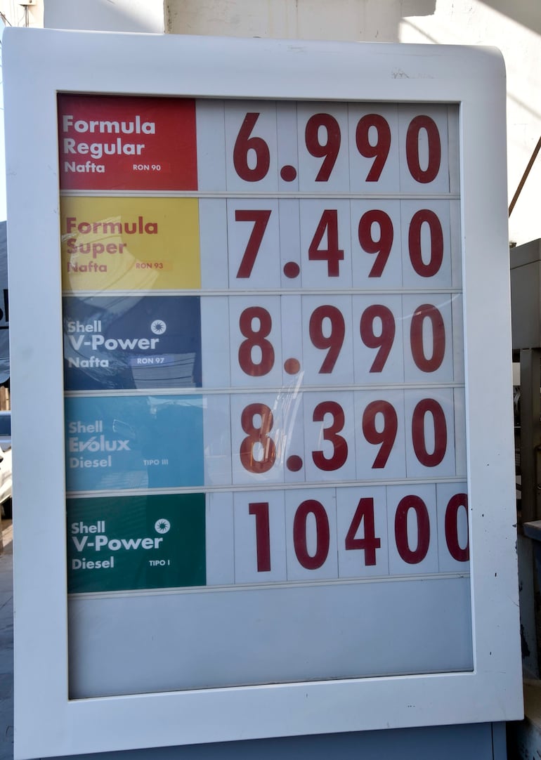 Cartel de precios de combustibles en estación de servicio, mostrando precios de nafta y diésel en un ambiente urbano.