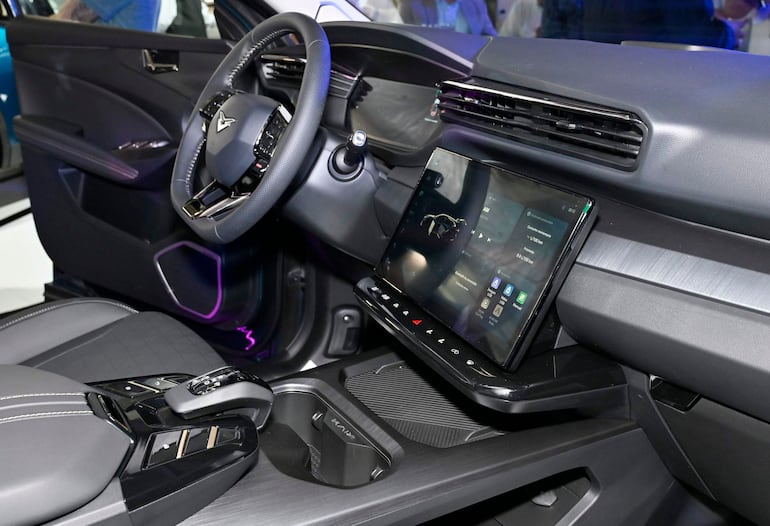 Interior de un automóvil moderno con volante con logotipo, pantalla de infoentretenimiento y luz ambiental púrpura.