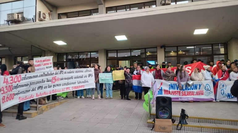 Manifestantes, mayormente mujeres, sostienen pancartas y un gran banner exigiendo mejoras salariales frente a un edificio gubernamental.