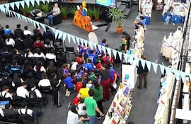 Grupo de jóvenes sentados en el suelo, escuchando a dos oradores en un escenario decorado con libros y banderines de colores.