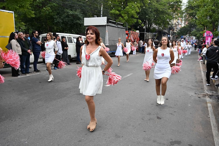 Seis mujeres vestidas de blanco, moviéndose alegremente con pompones rosa en un evento al aire libre.