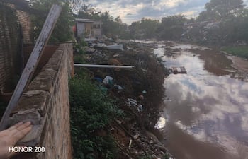 Paisaje urbano deteriorado con desechos alrededor de un canal de agua contaminada, estructuras abandonadas y cielo nublado.
