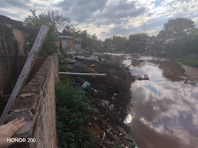 Paisaje urbano deteriorado con desechos alrededor de un canal de agua contaminada, estructuras abandonadas y cielo nublado.