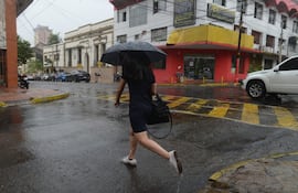 Un hombre se protege de la lluvia con un paraguas mientras cruza una calle en el microcentro de Asunción.