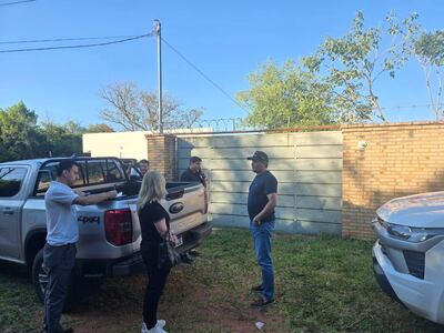 Hombre en camisa blanca toma notas, mientras mujer rubia escucha en patio despejado con cielo azul.
