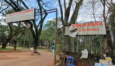 Edificio de acceso a la Policía Nacional en Alto Paraná, con letreros desgastados y rodeado de árboles altos.