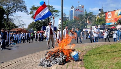 Médicos en batas blancas sosteniendo una bandera de Paraguay, con una fogata ardiente en el centro de la manifestación.