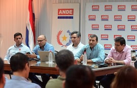 Hombres sentados tras mesa, discutiendo; uno usa micrófono. Banderas de Paraguay y banner de ANDE al fondo.