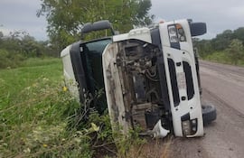 Camión volcado en la orilla de una carretera rural con cielo nublado y vegetación densa alrededor.