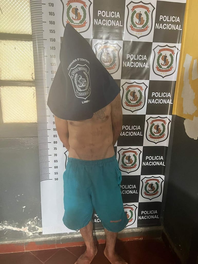 Hombre de 32 años con capucho oscuro y pantalones cortos azules, detenido en comisaría sin otros presentes.