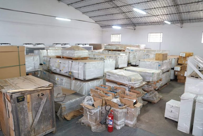 Almacén lleno de cajas apiladas y un extintor visible, bajo luz artificial en un espacio de almacenamiento.