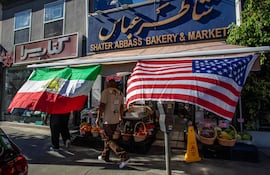 Un hombre camina por un mercado iraní con una bandera iraní y una estadounidense afuera de la tienda en la Plaza Persa en el vecindario de West LA en Los Ángeles.