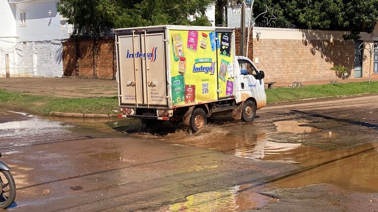 Camión colorido de Indega salpicando agua en un charco en una calle pavimentada sin personas visibles.