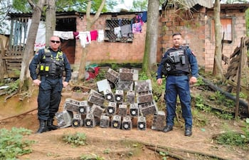 Dos policías nacionales en uniformes tácticos observan máquinas desmanteladas en un entorno residencial rústico.