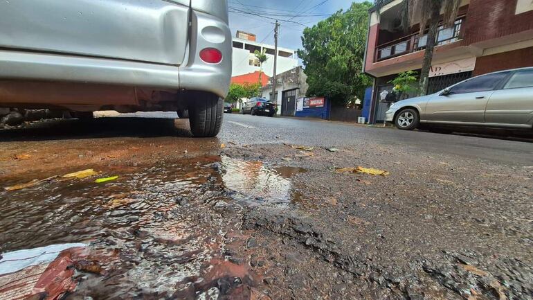 Calle tranquila con vehículos estacionados y un charco de agua reflejando edificios en Encarnación.