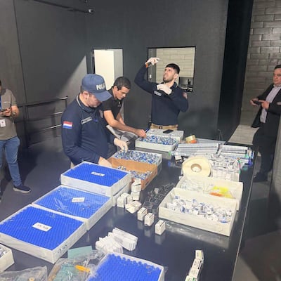 Hombres en laboratorio, uno con gorra de 'POLICÍA' manipulando cajas, otro organizando materiales y un tercero usando un dispositivo.