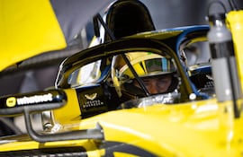 Joshua Duerksen en casco amarillo concentrado, sentado en su auto de carreras amarillo, preparándose para iniciar una prueba.