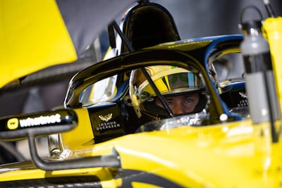 Joshua Duerksen en casco amarillo concentrado, sentado en su auto de carreras amarillo, preparándose para iniciar una prueba.