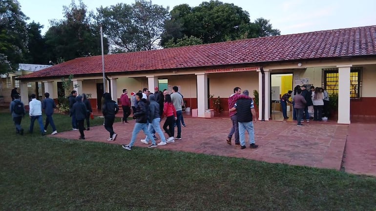 Grupo de personas conversando frente al colegio, con atuendos informales y un ambiente vespertino.