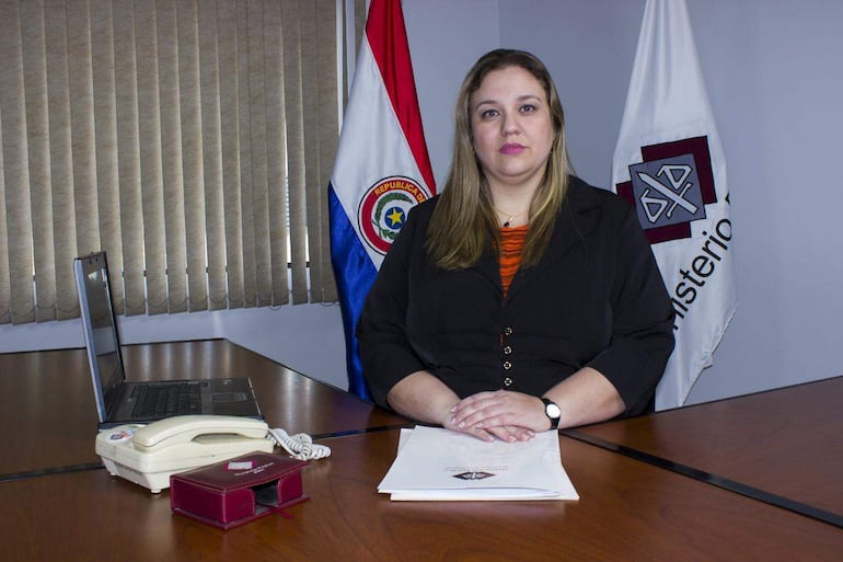 Viviana Stella Duarte Bojanovich con blusa negra, cabello lacio, sentada ante un escritorio con bandera de Paraguay y computadora portátil.