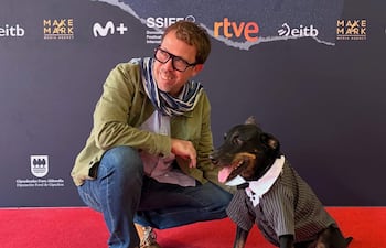 Marcelo Martinessi sonríe, arrodillado junto a su perro vestido a rayas en un ambiente festivo del Festival de San Sebastián.