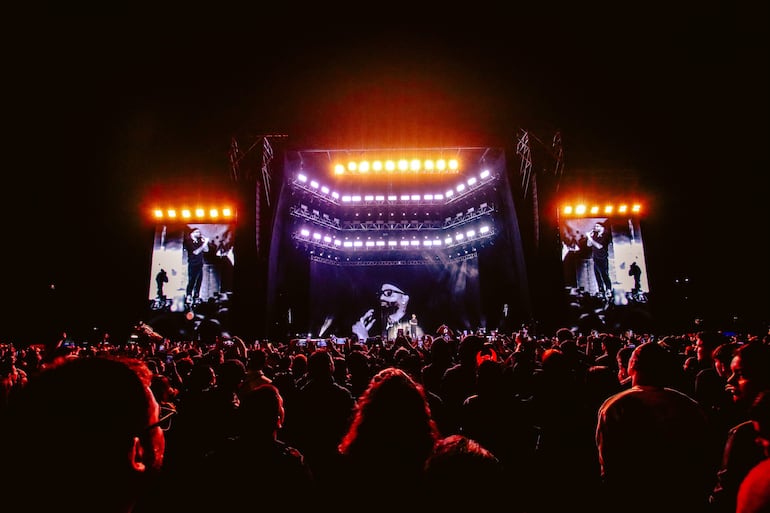 Multitud de asistentes mirando hacia el escenario iluminado, con teléfonos en mano, disfrutando del concierto de Arcángel.