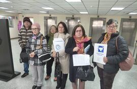 Seis enfermeras, algunas con documentos, en el Palacio de Justicia, una lleva bufanda de colores y otra sostiene un cartel de la Asociación Paraguaya de Enfermería.