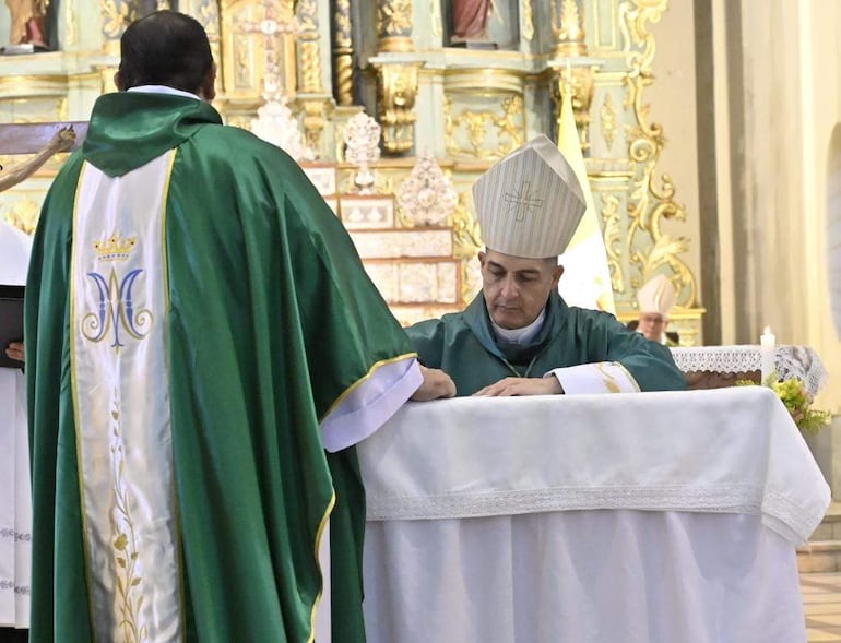 Un sacerdote de espaldas y el obispo Gabriel Escobar en un ambiente solemne, rodeados de otros clérigos en la ceremonia religiosa.