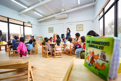 Grupo de niños con ropa colorida escucha a un adulto en aula iluminada, con un libro sobre animales en primer plano.