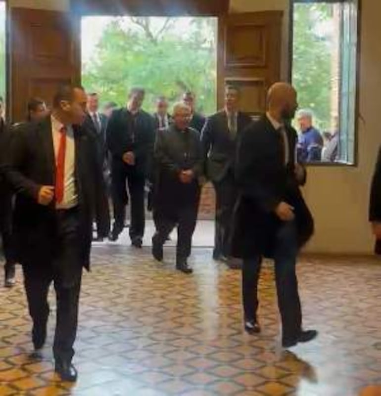 Grupo de hombres vestidos de traje en un salón iluminado, caminando hacia una reunión con expresiones tranquilas.