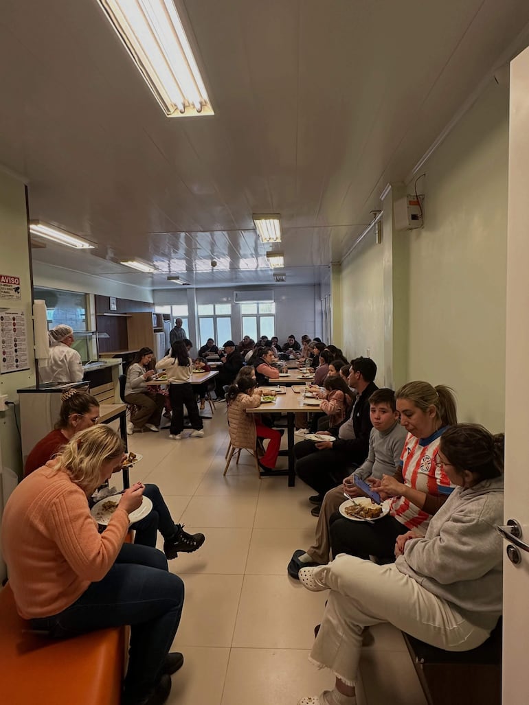 Comedor lleno de personas, algunas con expresiones tristes, otros felices, en un ambiente iluminado y casual.