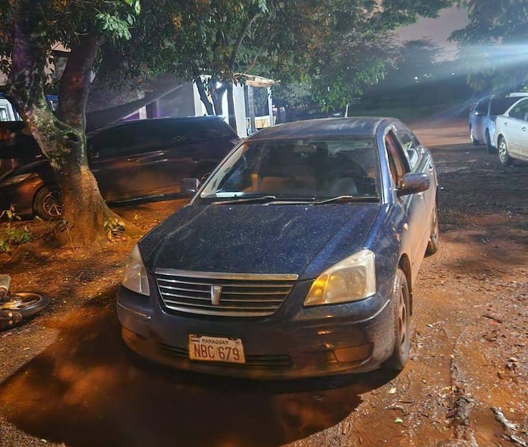 Vehículo oscuro con matrícula PARAGUAY NBC 679 estacionado bajo un árbol, sin personas visibles alrededor.