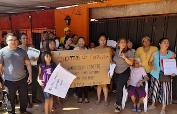 Grupo de 15 personas de pie y sentadas, con mujer mayor en el centro y niña con cartel que dice 'No nos saquen nuestra casa'.