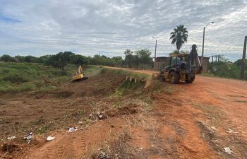 Máquinas de construcción amarillas operan en terreno rojo, con operador visible en una excavadora y cielo nublado.