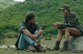 Jacob Elordi y Margaret Qualley sentados en una roca, conversando en un paisaje montañoso, ambos con vestimenta informal.
