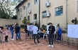 Niño con camiseta a rayas, adultos conversando, mujer en mesa informativa. Ambiente de actividad electoral al aire libre.