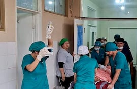 Seis médicos en uniformes quirúrgicos verdes, activo en el pasillo del hospital, asisten a un paciente en camilla.