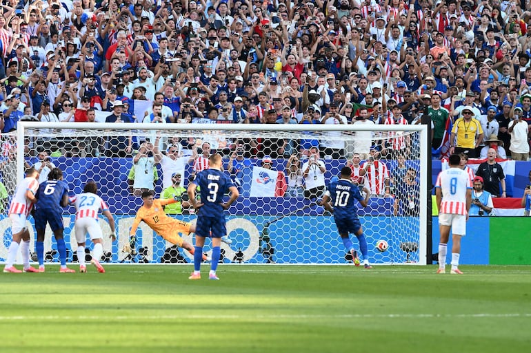 Jugador número 10 en camiseta azul ejecutando un penal frente al portero número 12 en un estadio con tribunas llenas.