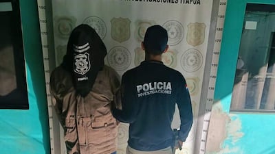 Hombre con capucha de tono marrón es detenido por agente policial con chaqueta negra en sede policial.