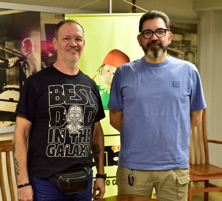 Tito Ibarrola con camiseta negra 'BEST DAD IN THE GALAXY' y bolso negro, sonríe junto a Tony Apuril en camiseta azul claro.