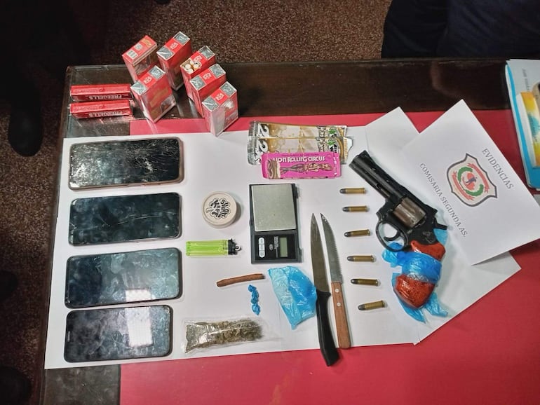 Objetos incautados en la operación: teléfonos móviles dañados, un revólver negro, cuchillos y sustancias sospechosas sobre una mesa.