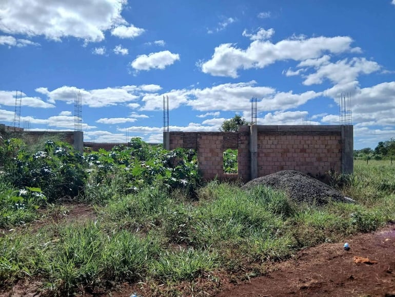 Terreno vacío con estructuras de ladrillo en construcción rodeadas de vegetación en un día despejado.