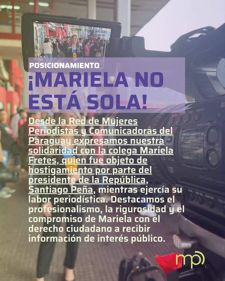 Grupo de personas en un evento con carteles apoyando a Mariela Fretes, con expresiones de solidaridad en un ambiente de conferencia.