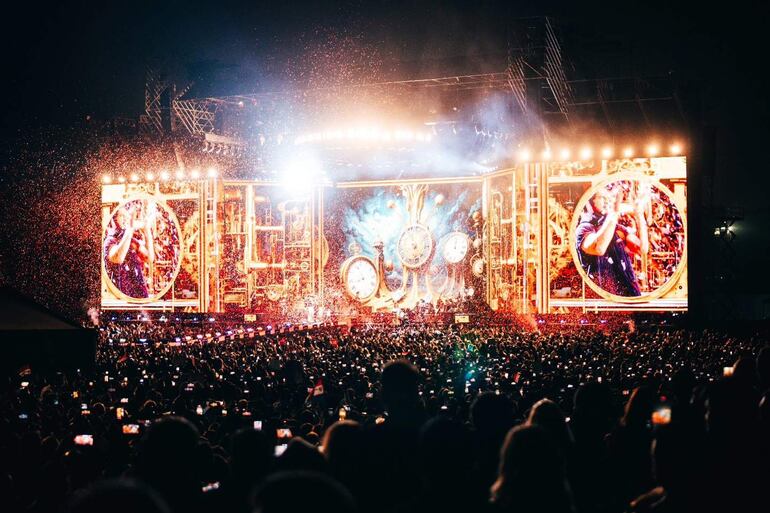 Escenario principal iluminado con confeti mientras la multitud sostiene teléfonos móviles. Ambiente festivo y dinámico.