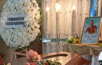 Altar funerario con ataúd de madera, corona de flores y velas encendidas en ambiente sobrio y respetuoso.
