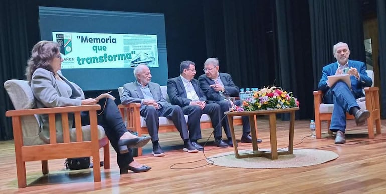 Guillermina Kanonnikoff en blazer gris, junto a sacerdotes en chaquetas, en un panel con fondo de telón que dice 'Memoria que transforma'.