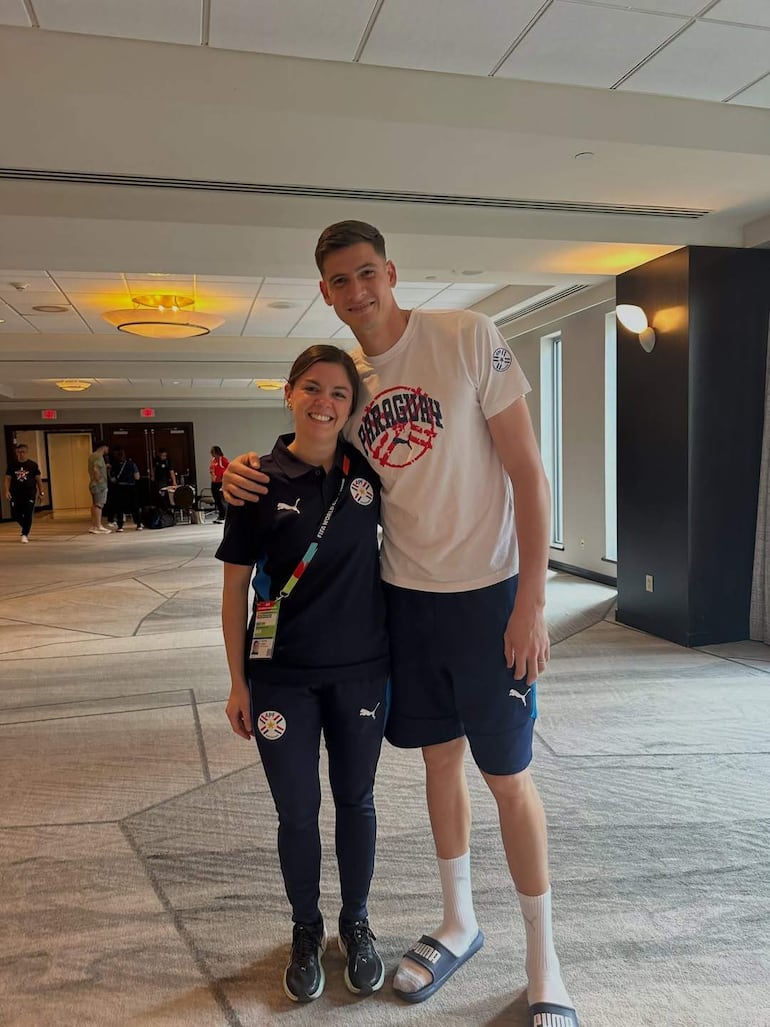 Mujer en camiseta oscura y hombre en camiseta blanca de Paraguay sonríen en ambiente iluminado, posando con camaradería.