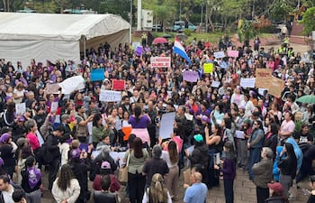 Multitud vestida de morado escucha atentamente a una mujer con micrófono en la plaza. Sostenían carteles con mensajes de protesta.