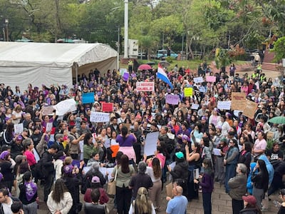 Multitud vestida de morado escucha atentamente a una mujer con micrófono en la plaza. Sostenían carteles con mensajes de protesta.
