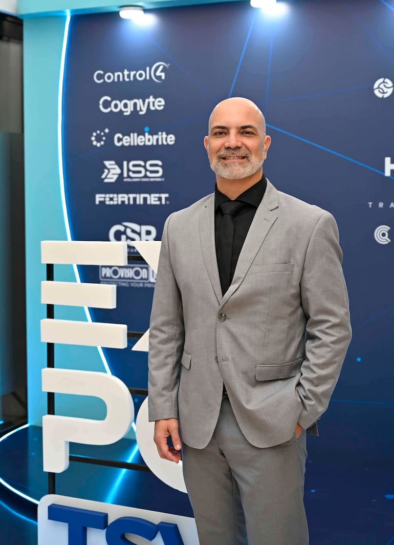 Hombre de pie, Ing. Pablo Salinas, sonríe en traje gris claro, rodeado de logotipos tecnológicos en un evento profesional.